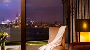 A cozy room with a view of a city skyline at night, featuring a comfortable chair, a small table with a cup of coffee, and a lamp. - Harbour Grand Hong Kong (Hong Kong)