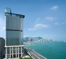 Un edificio alto con fachada de vidrio que da a un puerto concurrido con barcos y un puente.