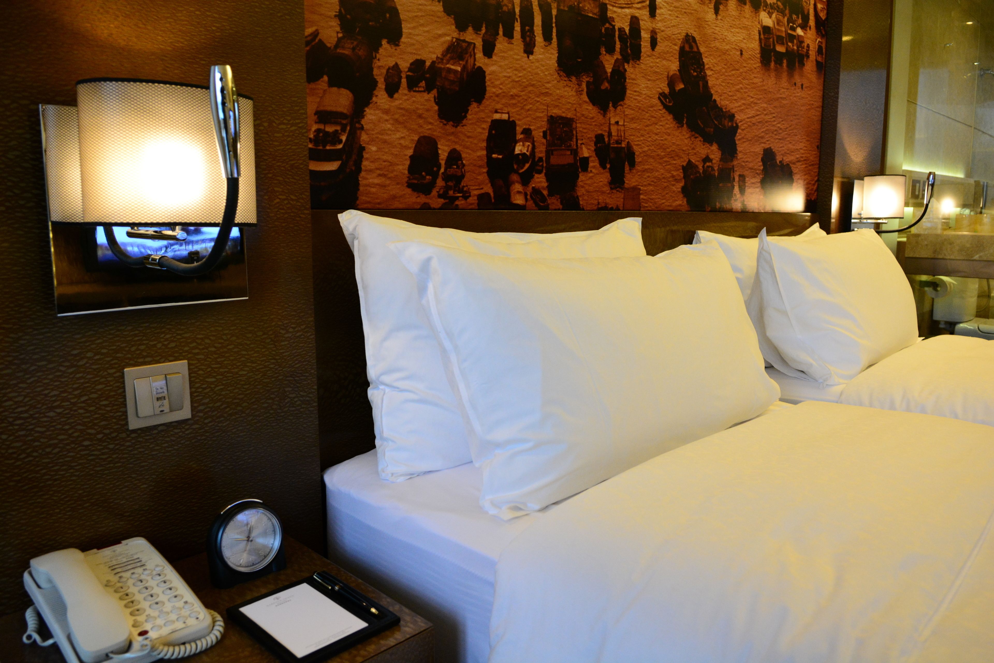 Habitación de hotel con una cama, teléfono empotrado en la pared, un reloj y una pared con textura.
