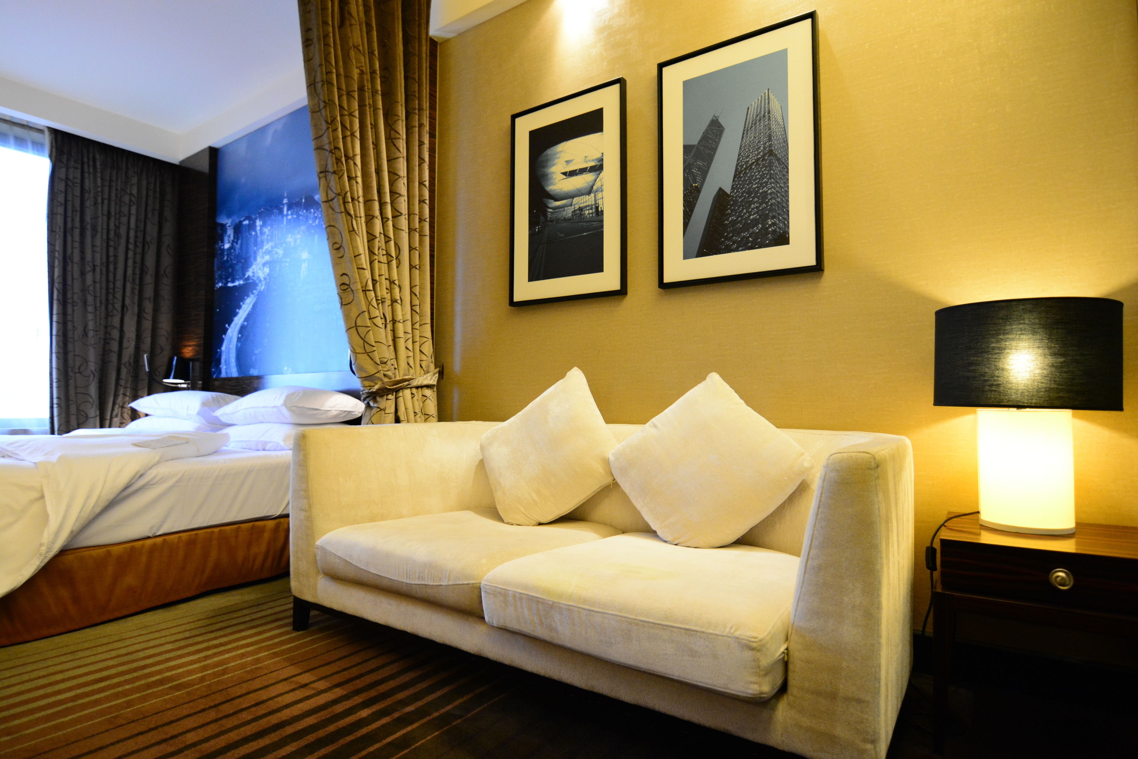 A hotel room with a bed, a sofa, a lamp, and two framed pictures on the wall.