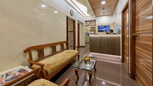 A hotel lobby with a wooden sofa, a glass coffee table, and a reception desk. - Hotel Royal Castle (Mumbai)