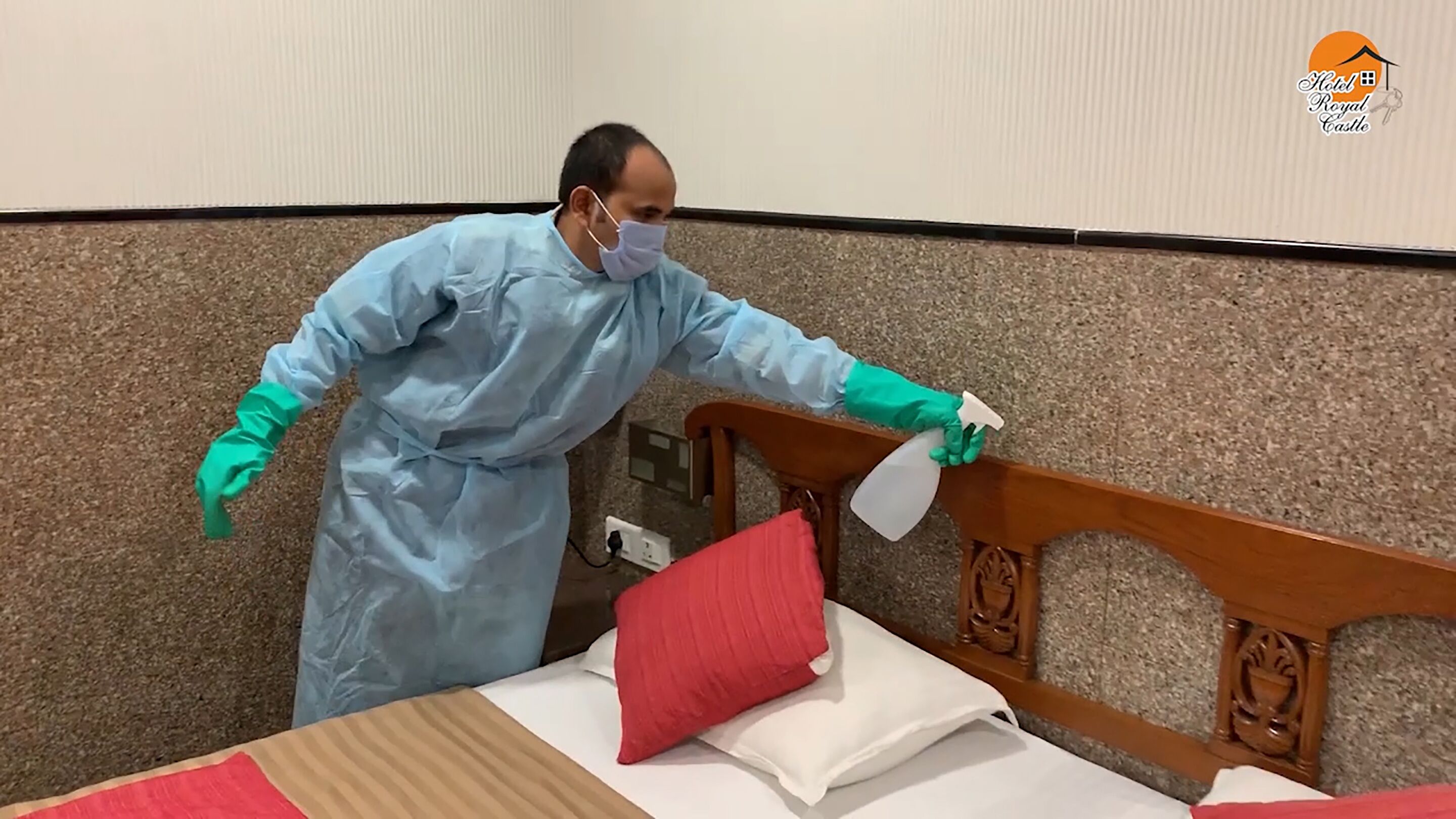 Una persona con un traje azul de protección limpiando una cama con un atomizador.
