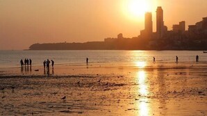 A beach with people and birds during sunset, with buildings in the background. - Hotel Royal Castle (Mumbai)