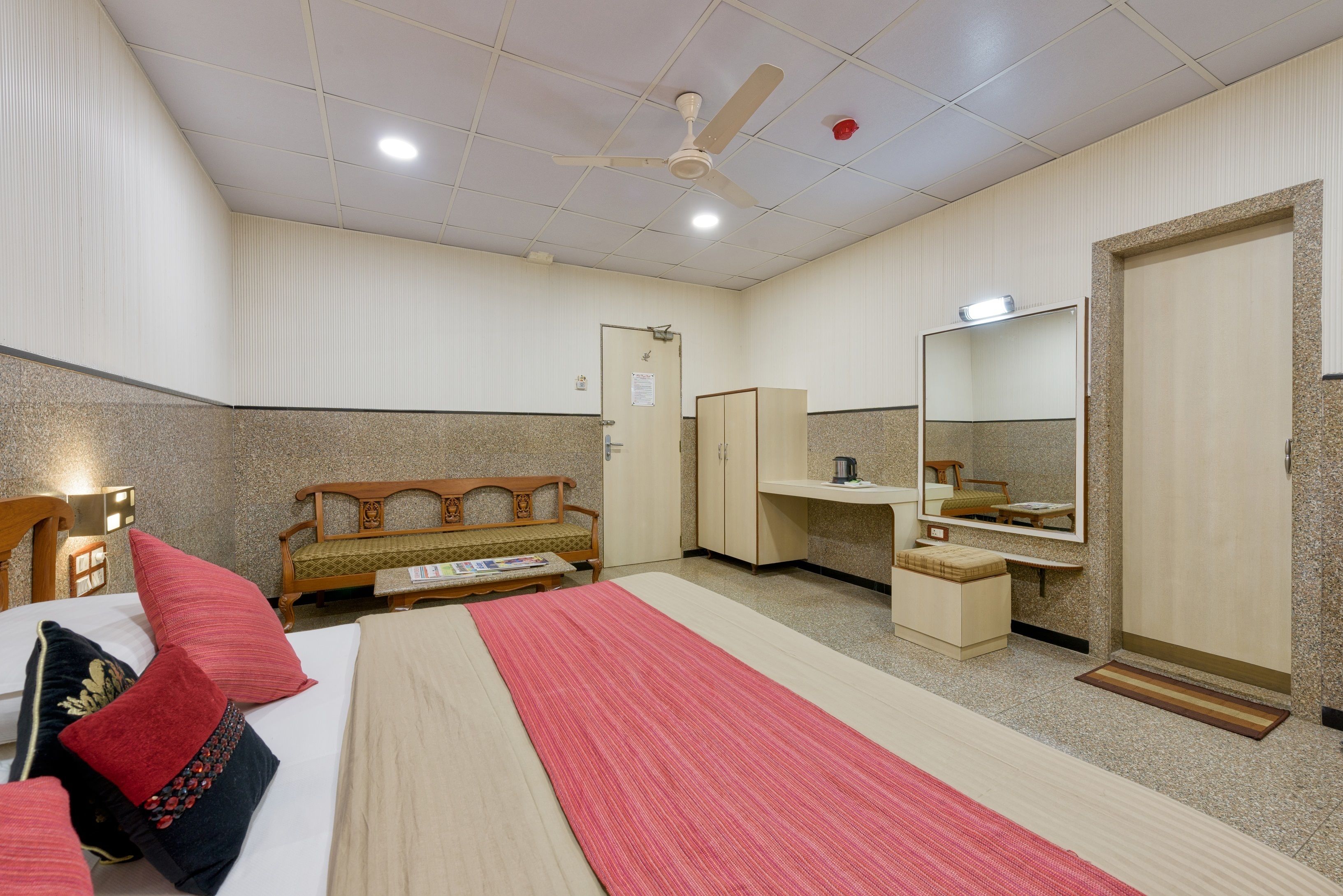 A hotel room with a bed, a desk, a wardrobe, a mirror, and a ceiling fan.