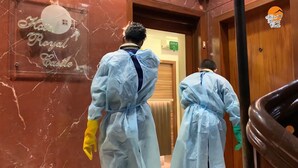 Two individuals in protective suits walking down a hallway with a sign reading "Hotel Royal Castle". - Hotel Royal Castle (Mumbai)