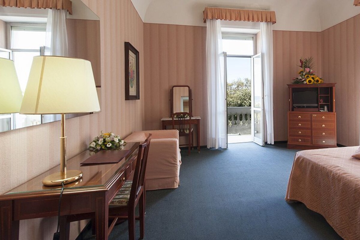 Una habitación de hotel con escritorio, silla, cama, cómoda y balcón con vistas.