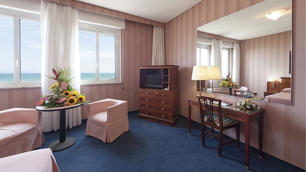 A hotel room with a bed, a desk with a chair, a dresser, a TV, and a large window with curtains. - Hotel Esplanade (Pescara)