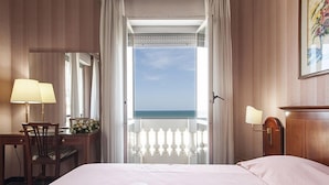 A hotel room with a bed, a desk with a lamp, a chair, and a view of the sea through a balcony. - Hotel Esplanade (Pescara)