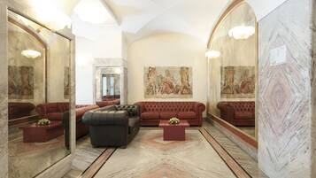 A luxurious lobby with marble flooring, red leather sofas, and classical wall paintings.