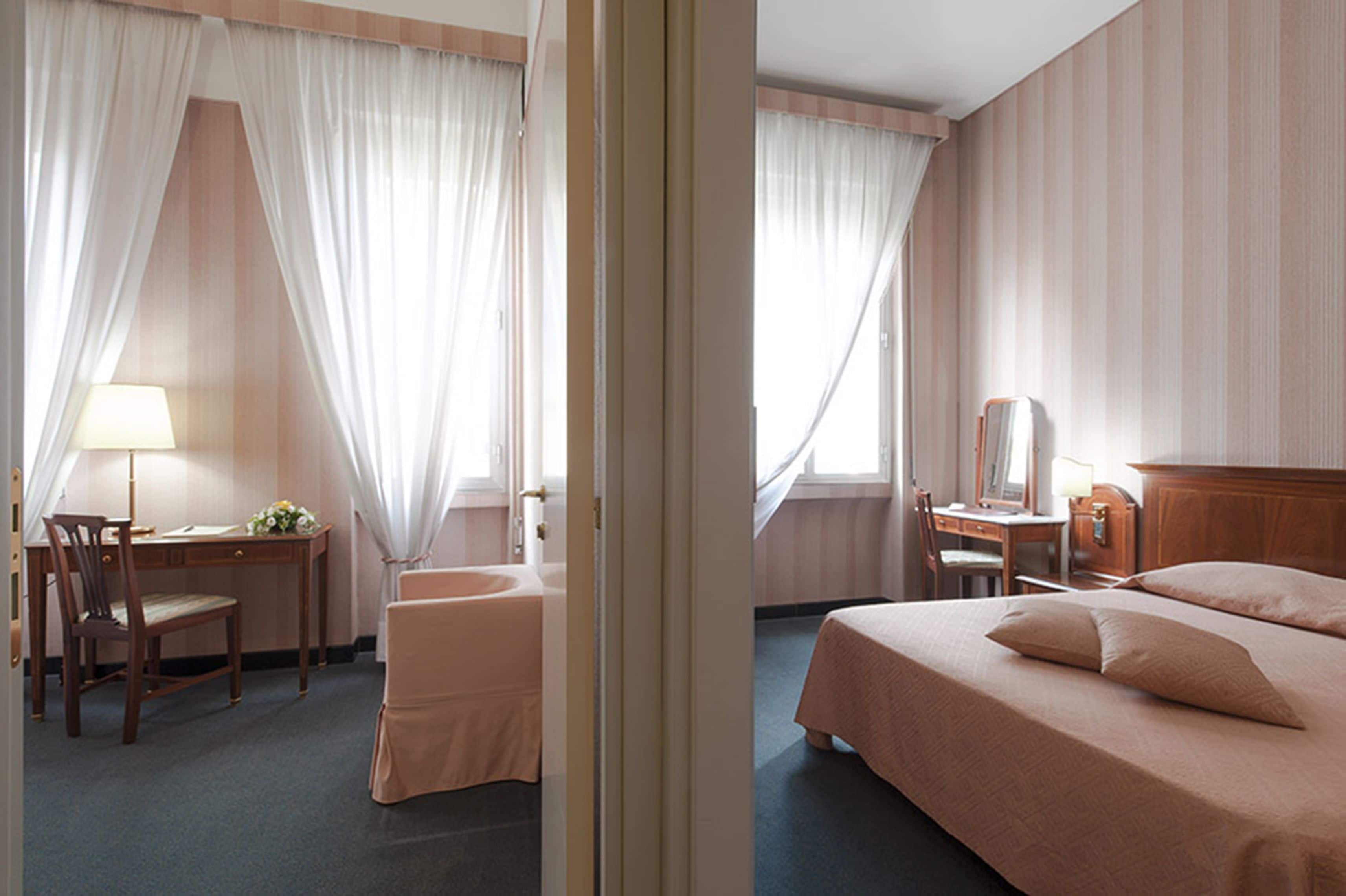Une chambre d’hôtel équipée d’un lit, d’un bureau, d’une chaise, d’une coiffeuse et d’une fenêtre avec des rideaux.