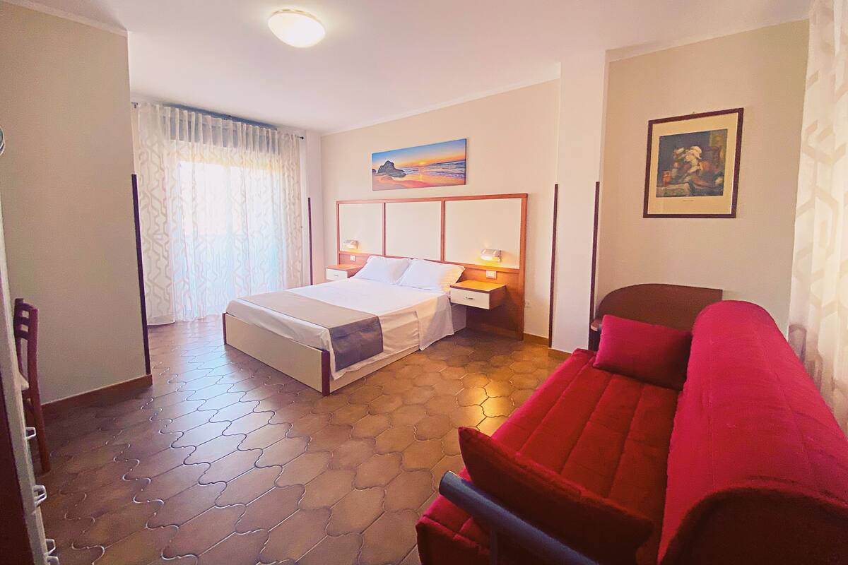A hotel room with a large bed, a red sofa, a painting on the wall, and a patterned floor.