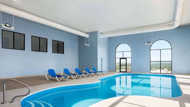 An indoor swimming pool with blue water, surrounded by blue lounge chairs and large arched windows.