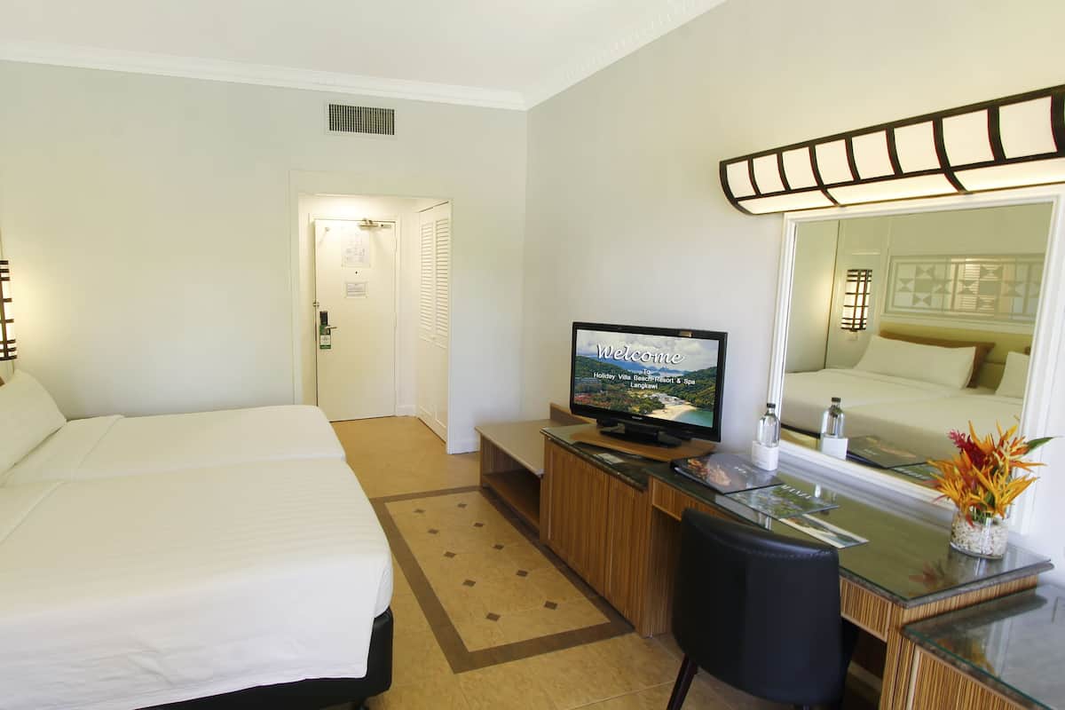 Une chambre d’hôtel avec deux lits, un bureau avec une télévision, un miroir et une petite table sur laquelle est posé un vase de fleurs.