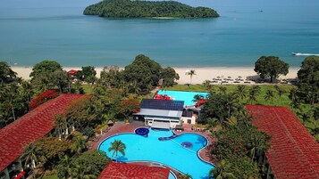 Un resort con una amplia piscina, acceso a la playa y exuberante entorno tropical.