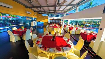 A spacious indoor dining area with multiple round tables covered with red tablecloths, surrounded by white chairs.