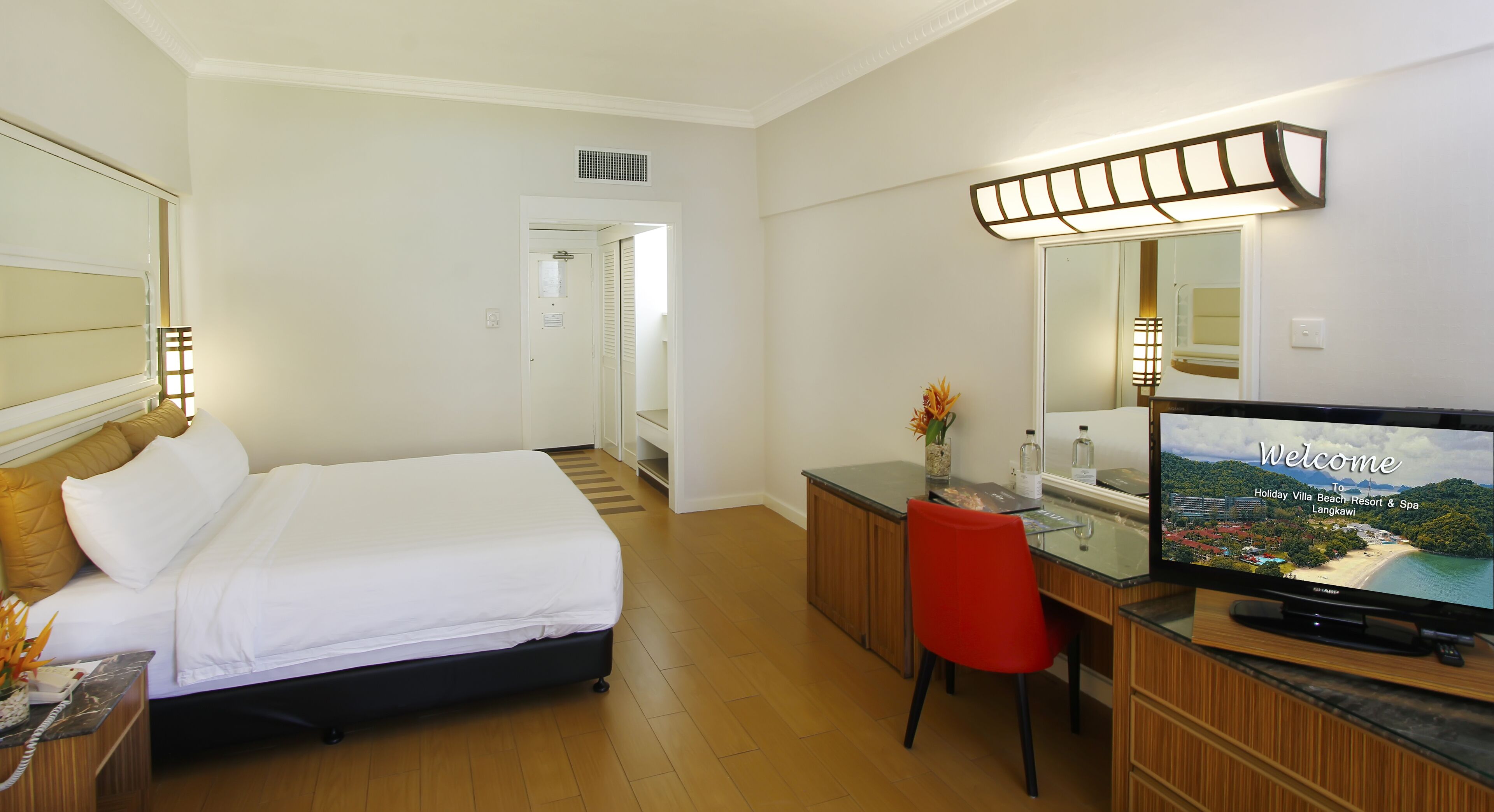 A hotel room with a bed, a desk with a TV, and a bathroom visible through an open door.