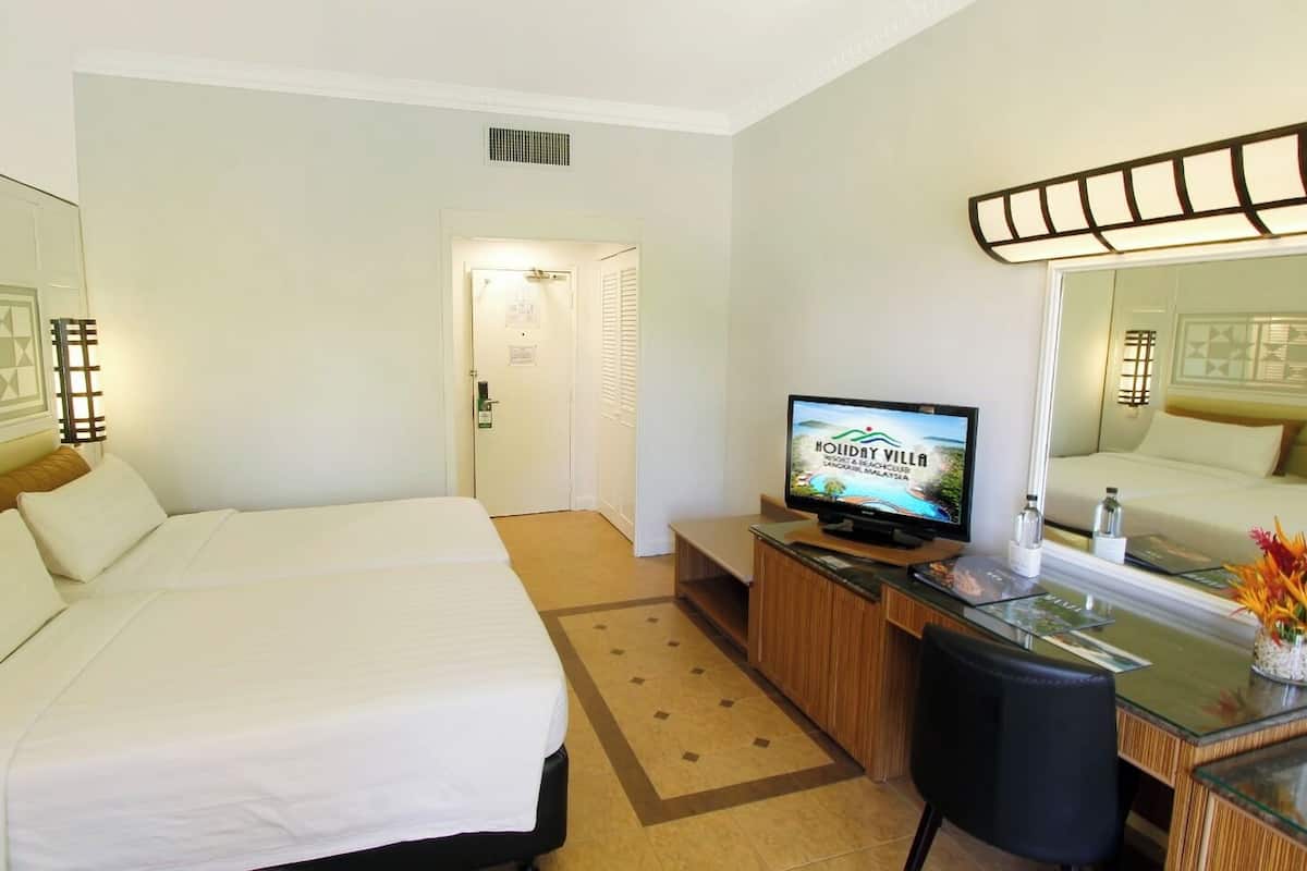 Habitació d'hotel amb dos llits, una taula de treball amb televisió, un mirall i un ram de flors decoratiu.