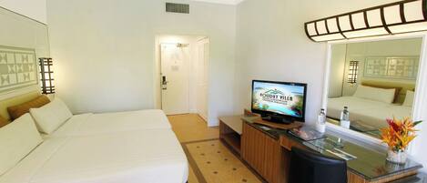 A hotel room with two beds, a desk with a television, a mirror, and a small table with a vase of flowers.