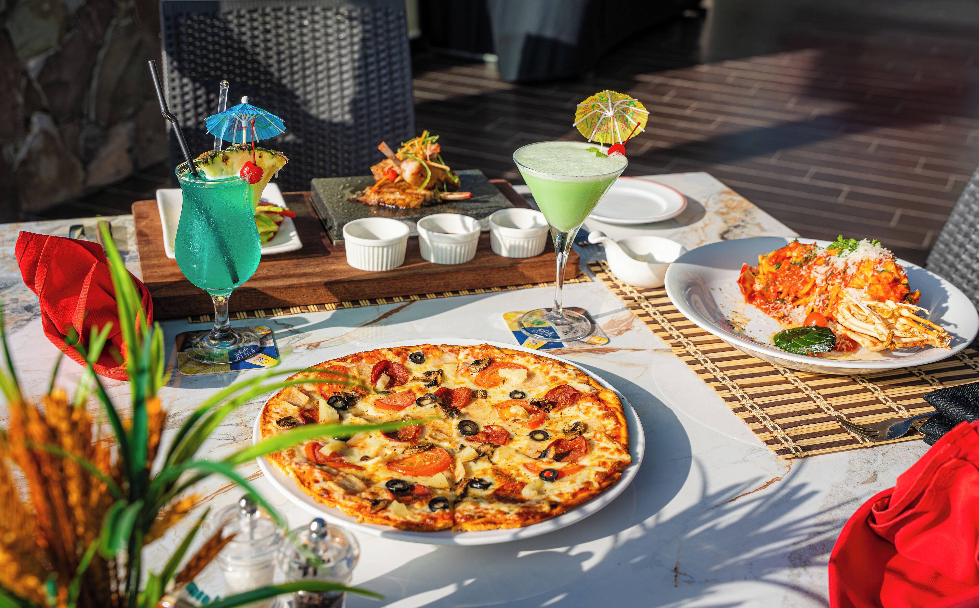 A table set with a pizza, a green cocktail, and a seafood dish.