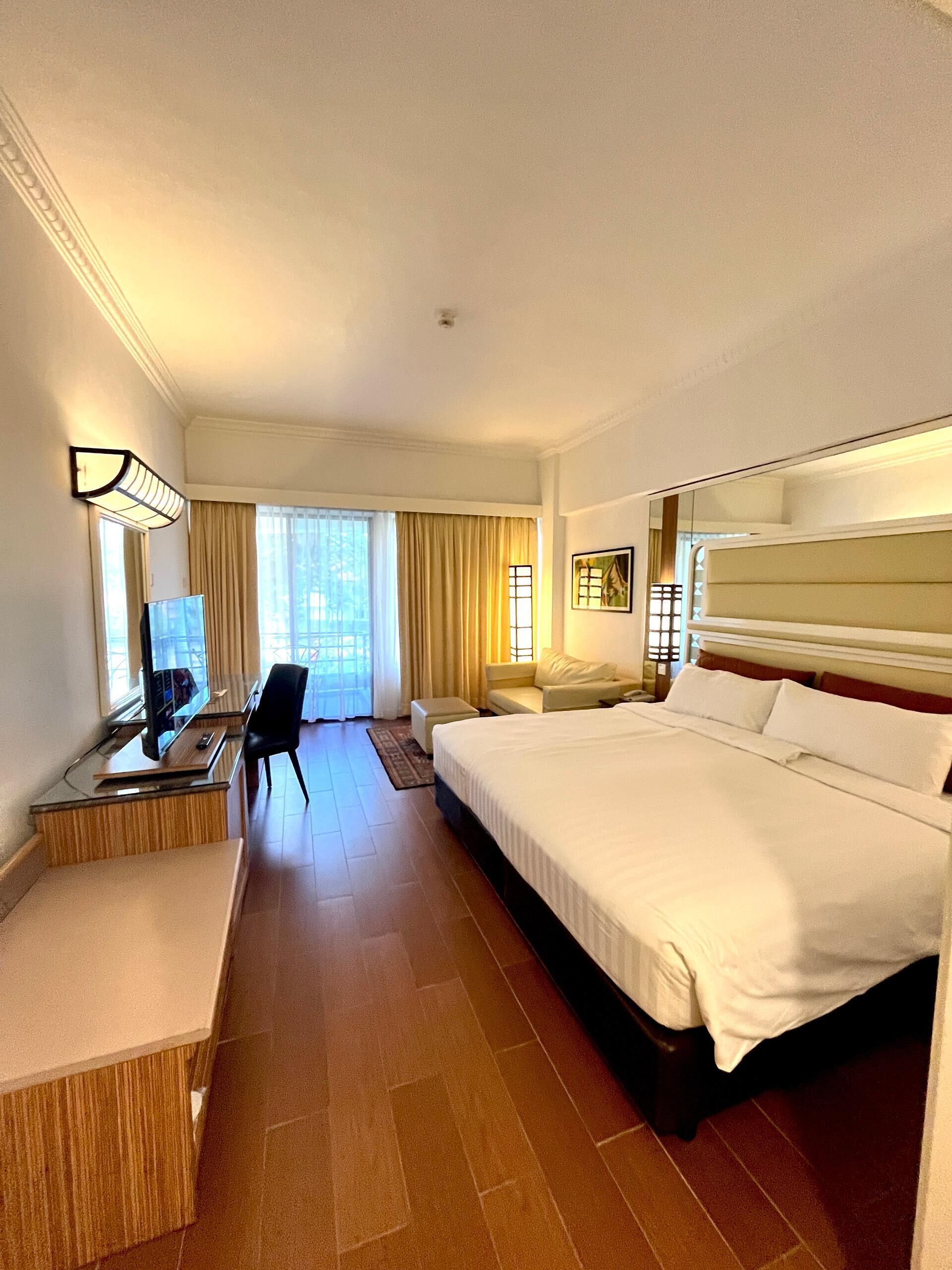 A hotel room with a large bed, a desk with a computer, a chair, and a sofa.
