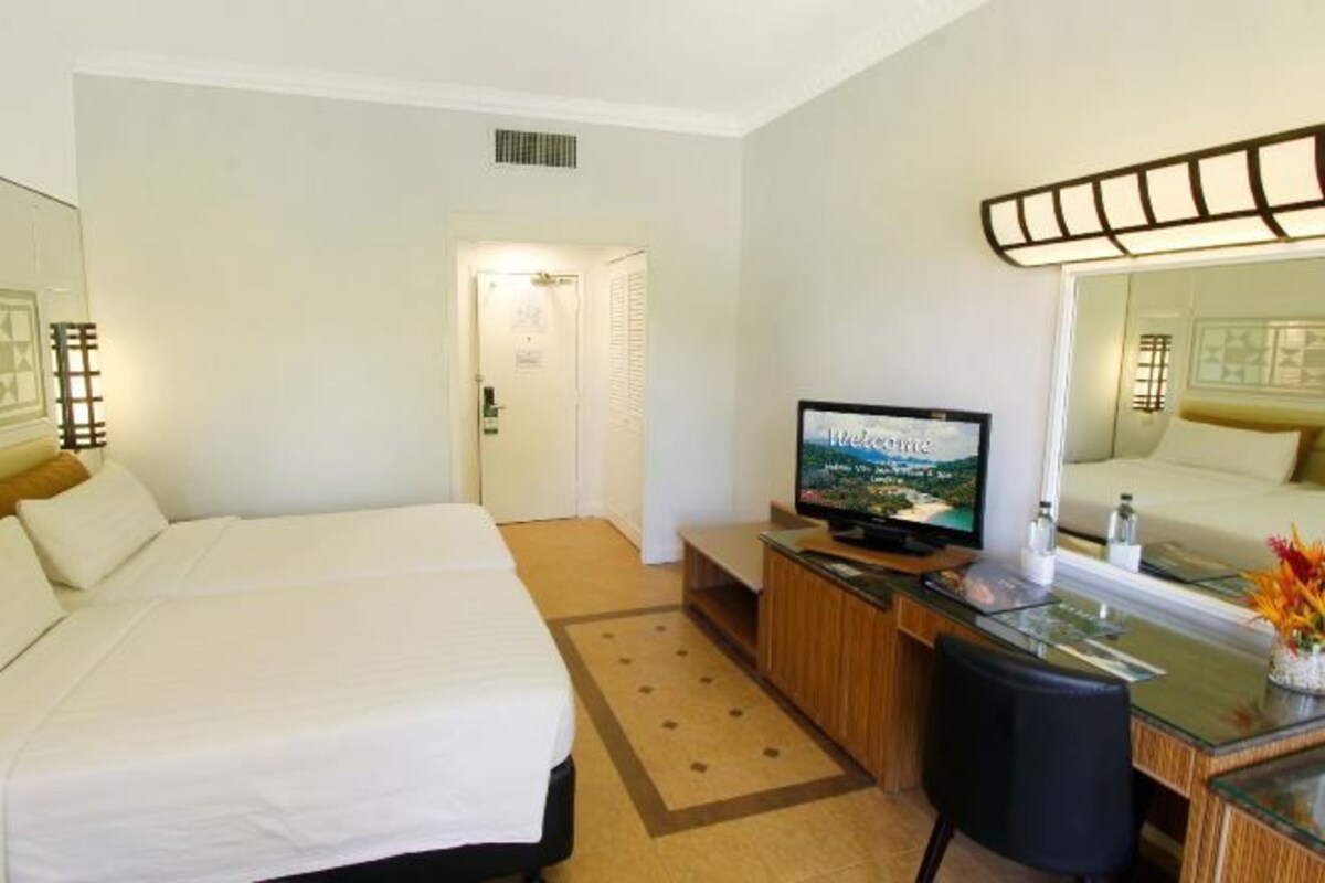 Een hotelkamer met twee bedden, een bureau en een televisie, en een spiegel.