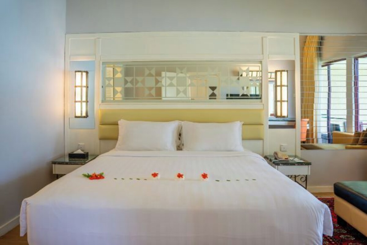 Een hotelkamer met een groot bed, nachtkastjes, een spiegel en een raam met gordijnen.