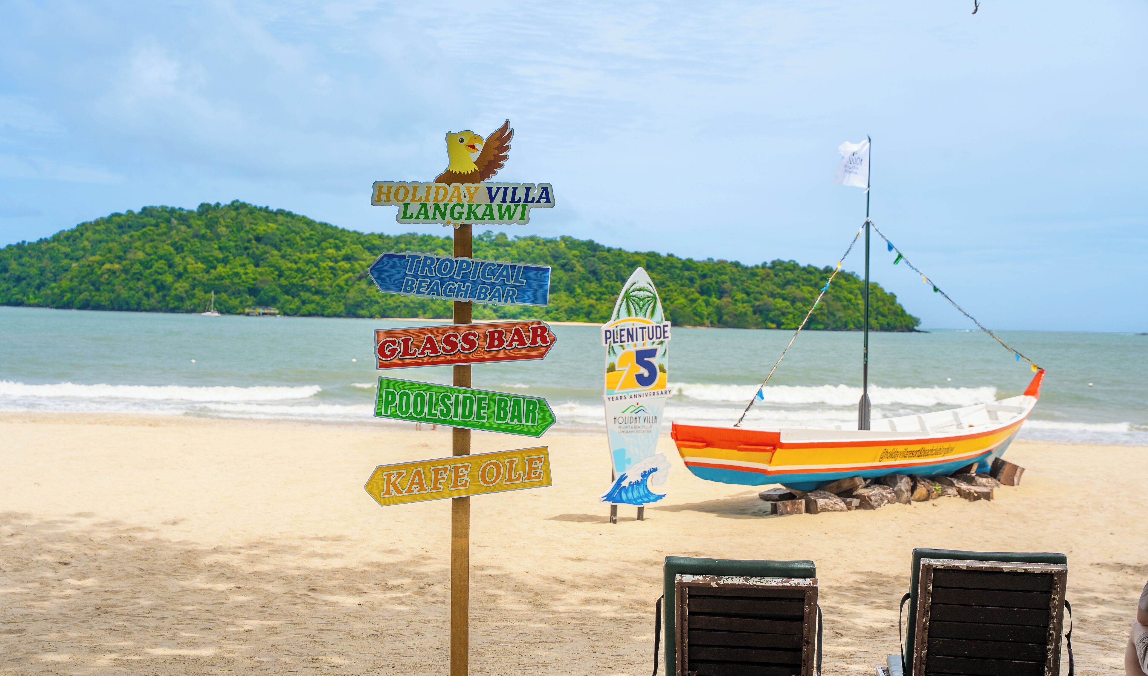 A beach with a signpost indicating various amenities including a tropical beach bar, glass bar, poolside bar, and kafiole. A boat is moored nearby, and a flag is flying.