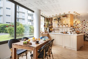 Una cocina moderna con una isla central, sillas de madera y un amplio ventanal con vistas a un edificio residencial y zonas verdes.