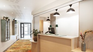 Un espace d’accueil avec un bureau en bois, deux lampes suspendues, une plante en pot et un vase rempli de fleurs.