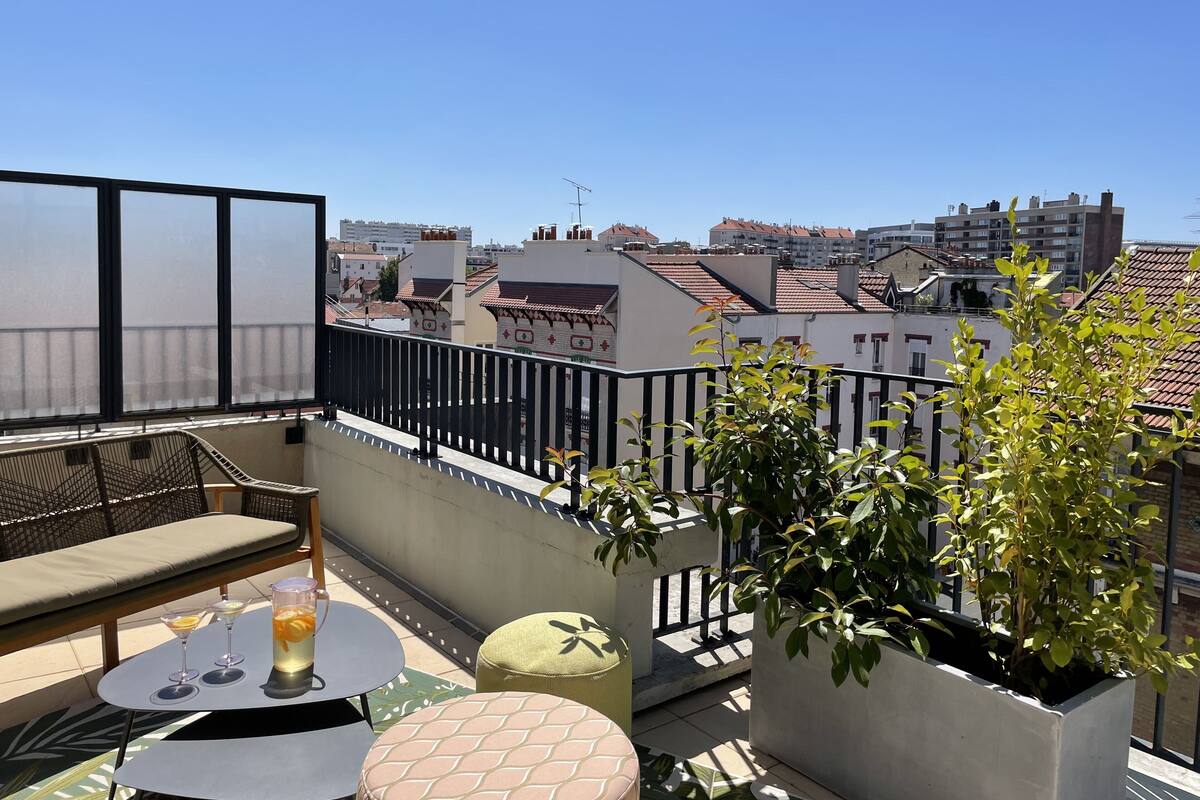 A balcony with a view of the city, a table with drinks, and outdoor seating.