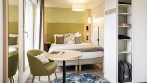 Une chambre d’hôtel avec un lit, une table ronde, une chaise, une armoire et une lampe.