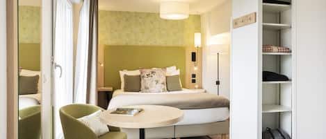 A hotel room with a bed, a round table, a chair, a wardrobe, and a lamp.