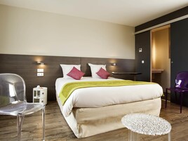 Quarto de hotel moderno com uma cama grande, uma mesinha de cabeceira, uma cadeira e uma escrivaninha.