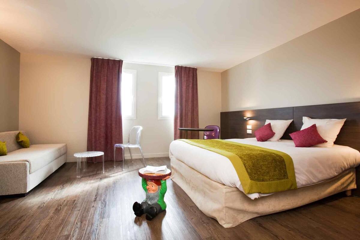 Et hotelværelse med seng, sofa, lille bord og stol.