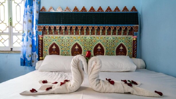 A bed with a decorative headboard, pillows, and towels arranged in a swan shape with rose petals.