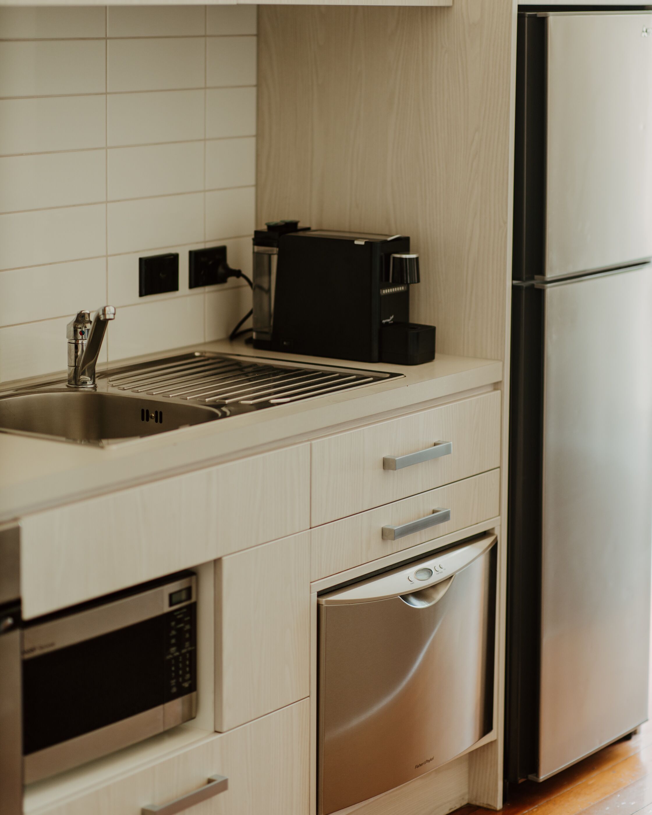 Una cocina moderna con un refrigerador de acero inoxidable, un horno empotrado, un microondas, una cafetera y un lavabo.
