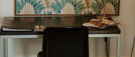 A desk with a laptop, a lamp, and a magazine, set against a wall with a tropical leaf pattern.