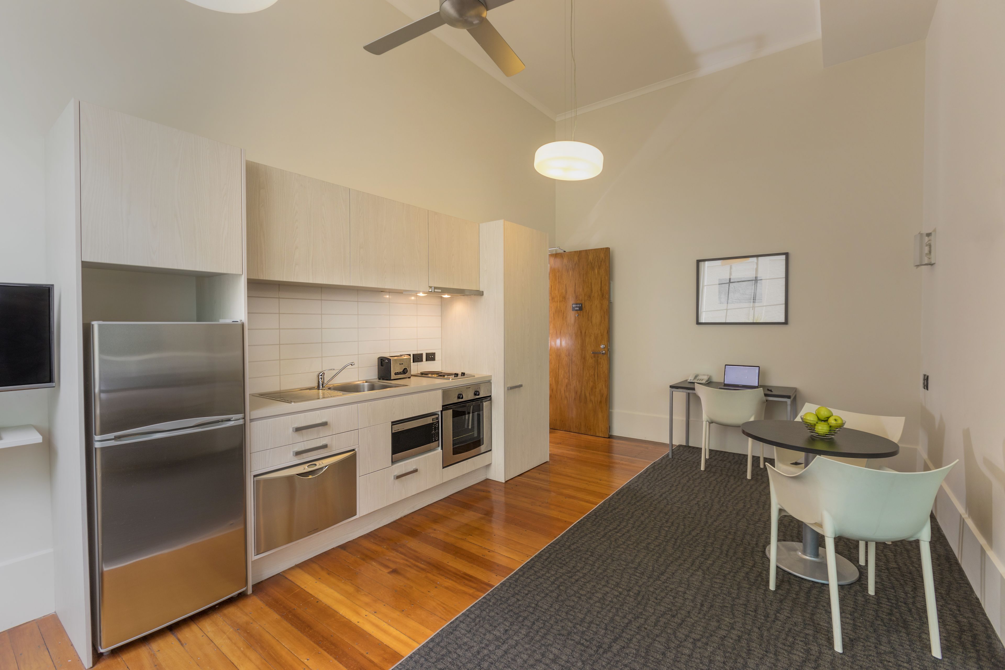 A modern kitchen with stainless steel appliances, a dining area with a table and chairs, and a ceiling fan.