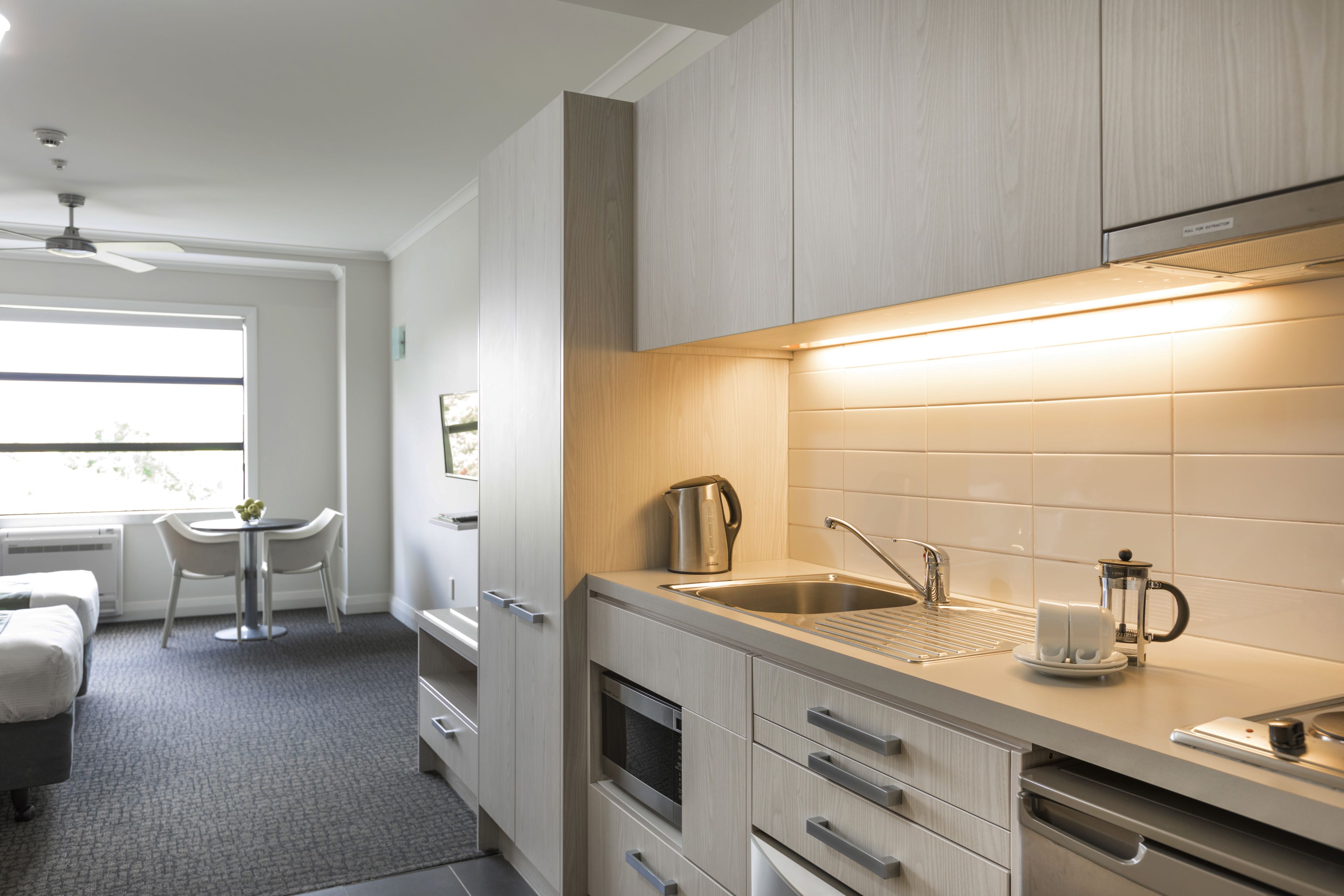 A modern kitchen with a built-in oven, a sink, and a coffee maker. There is a dining area with a table and chairs.