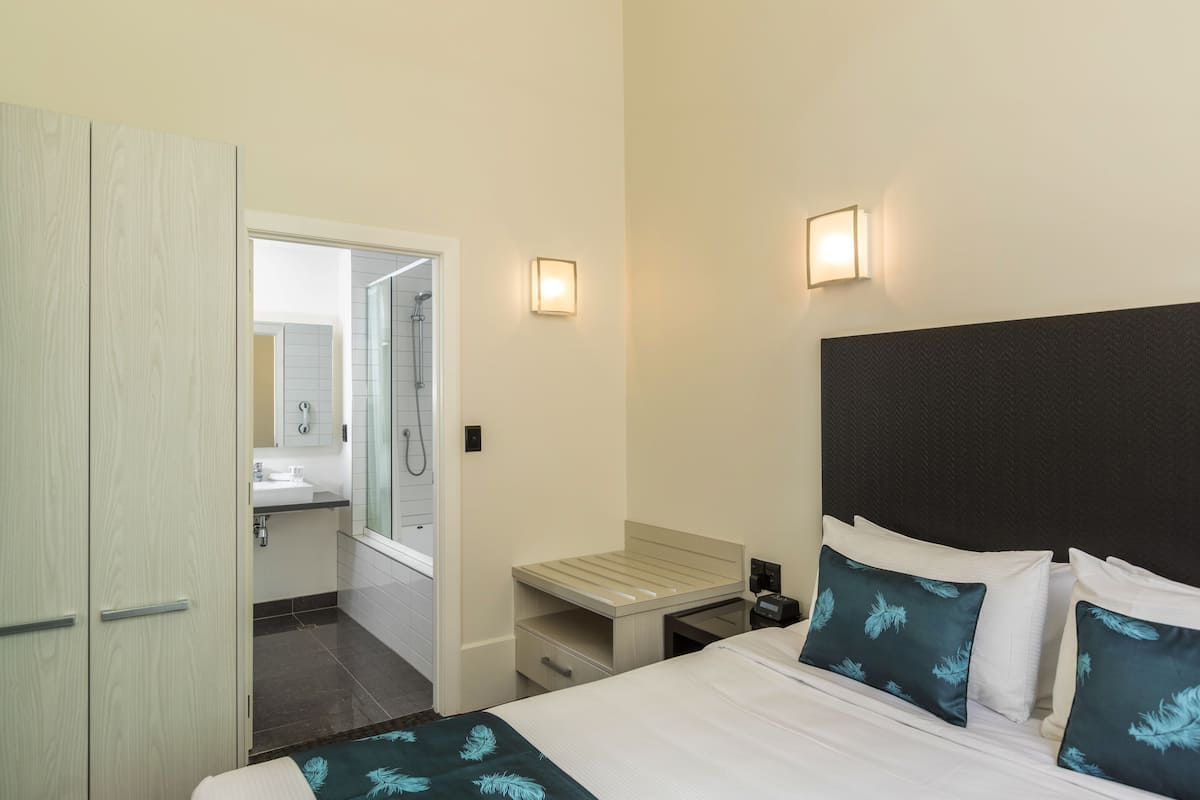 Quarto de hotel com cama, mesa de cabeceira e banheiro visível por uma porta aberta.