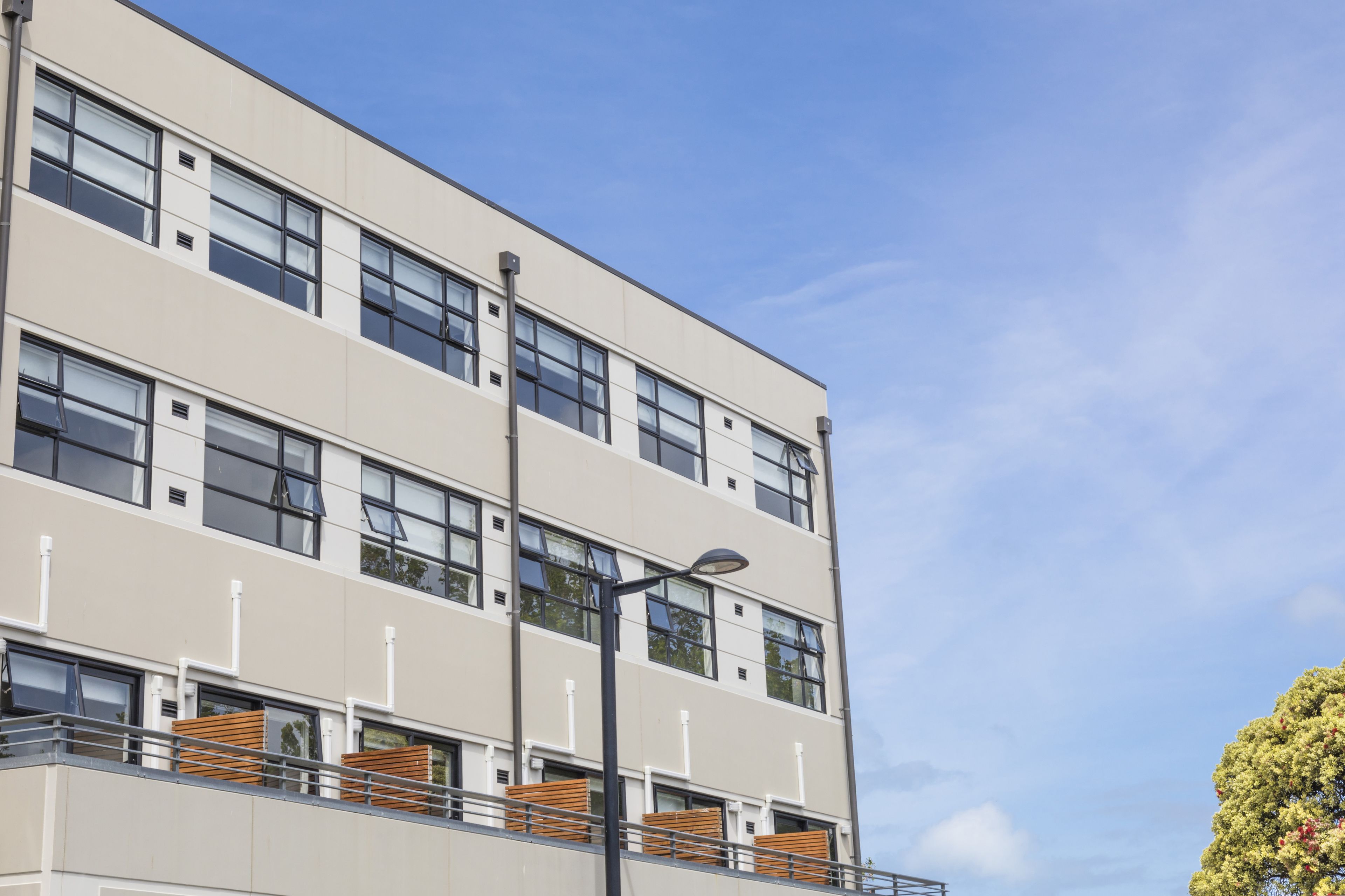 A multi-story building with large windows, balconies with wooden railings, and a clear sky.