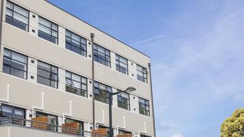A multi-story building with large windows, balconies with wooden railings, and a clear sky.