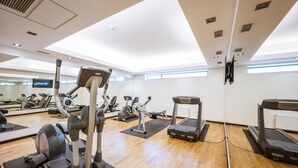 Une salle de sport équipée de divers appareils d’exercice, dotée d’un plancher en bois et de grandes fenêtres laissant entrer la lumière naturelle.