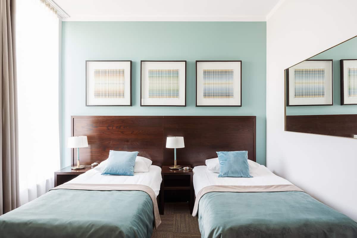 Ein Hotelzimmer mit zwei Betten, einem Holzkopfteil, gerahmten Kunstwerken an der Wand und einem Nachttisch mit einer Lampe.