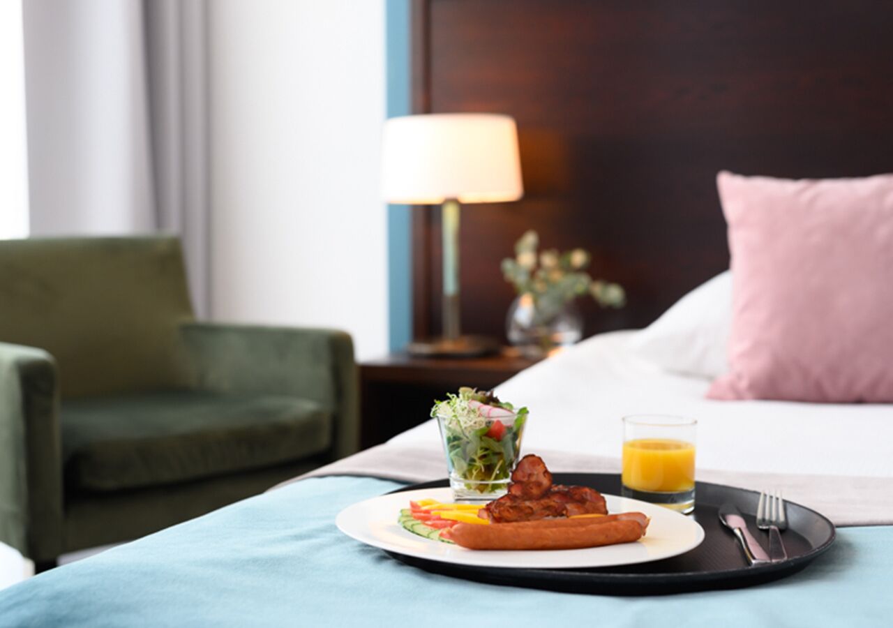 Un plateau de petit-déjeuner avec des œufs, du bacon, une salade et un verre de jus d’orange, posé sur un lit dans une chambre d’hôtel.