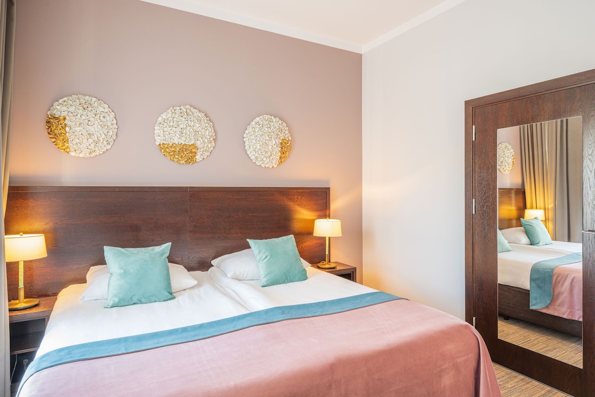 A hotel room with a large bed, two bedside lamps, a wooden headboard, and three wall-mounted decorative pieces.