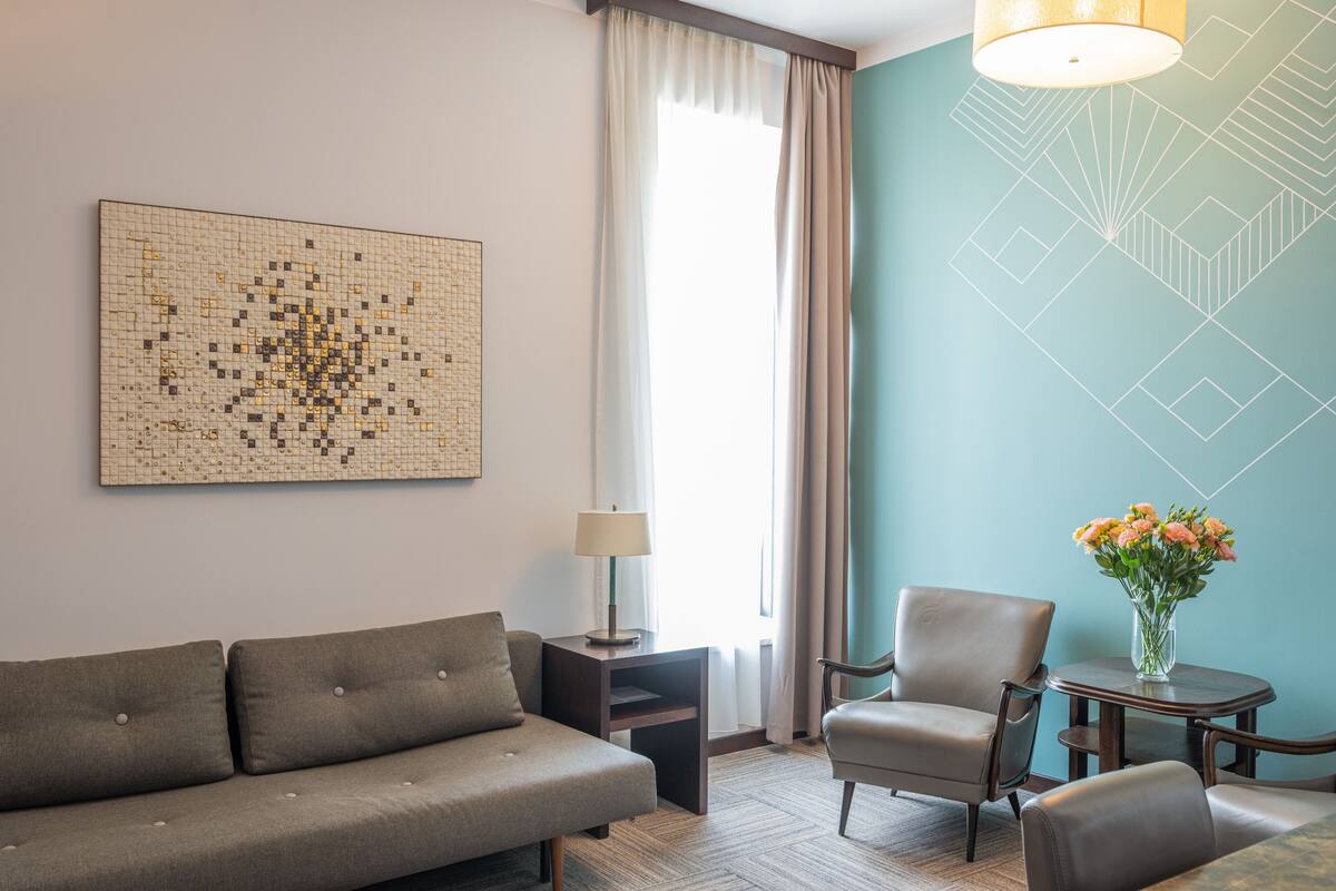Ein Hotelzimmer mit Sofa, Sessel, kleinem Tisch, Lampe und einer Wanddekoration.