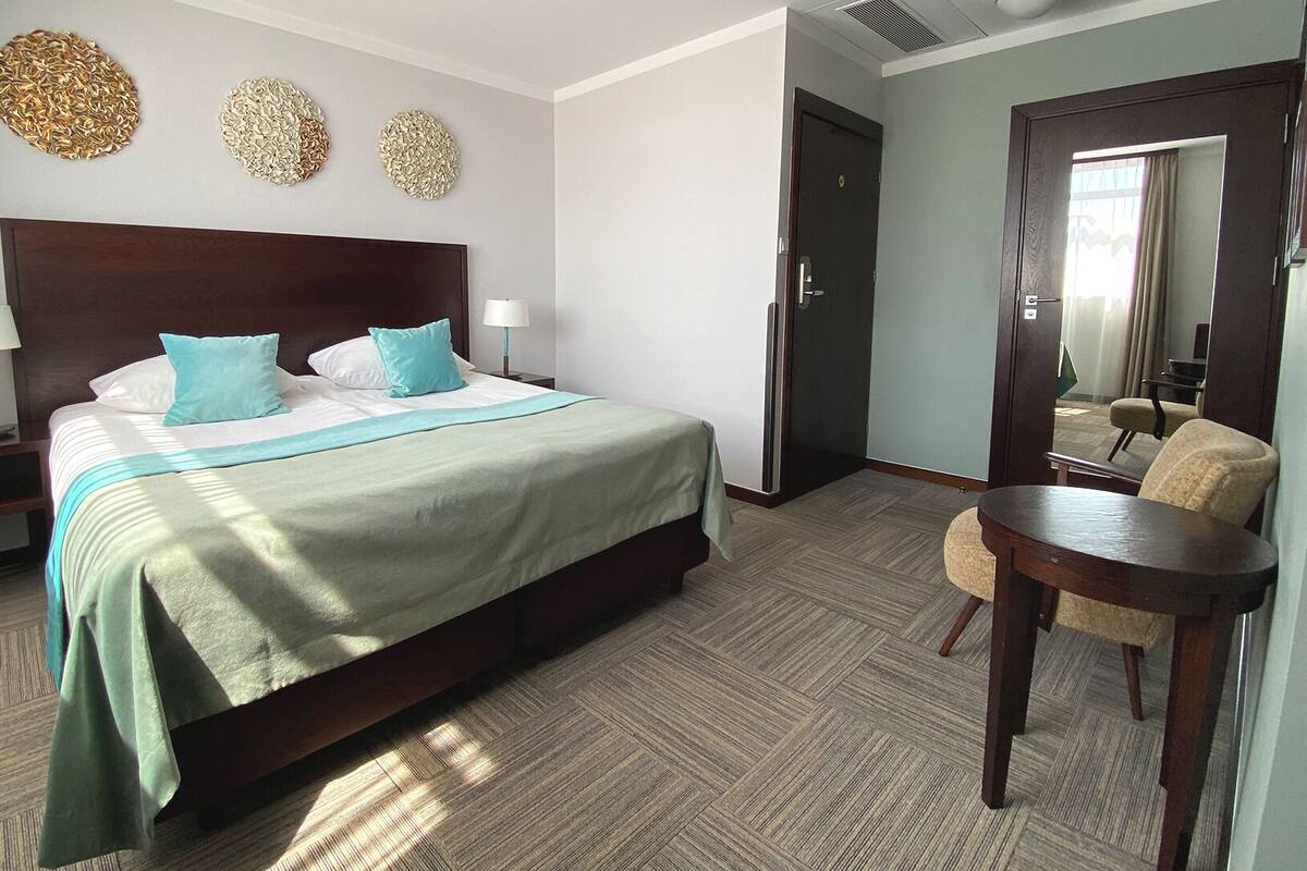 Ein Hotelzimmer mit einem großen Bett, zwei Nachttischen, einem Sessel und einem Spiegel.