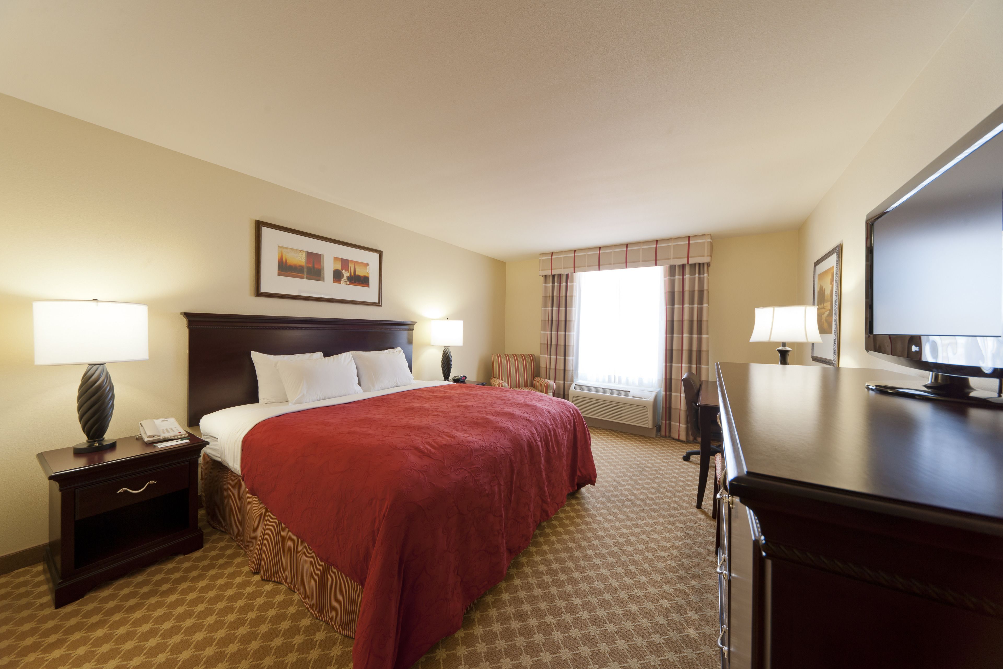 A hotel room with a large bed, two bedside tables with lamps, a television, and a window with curtains.