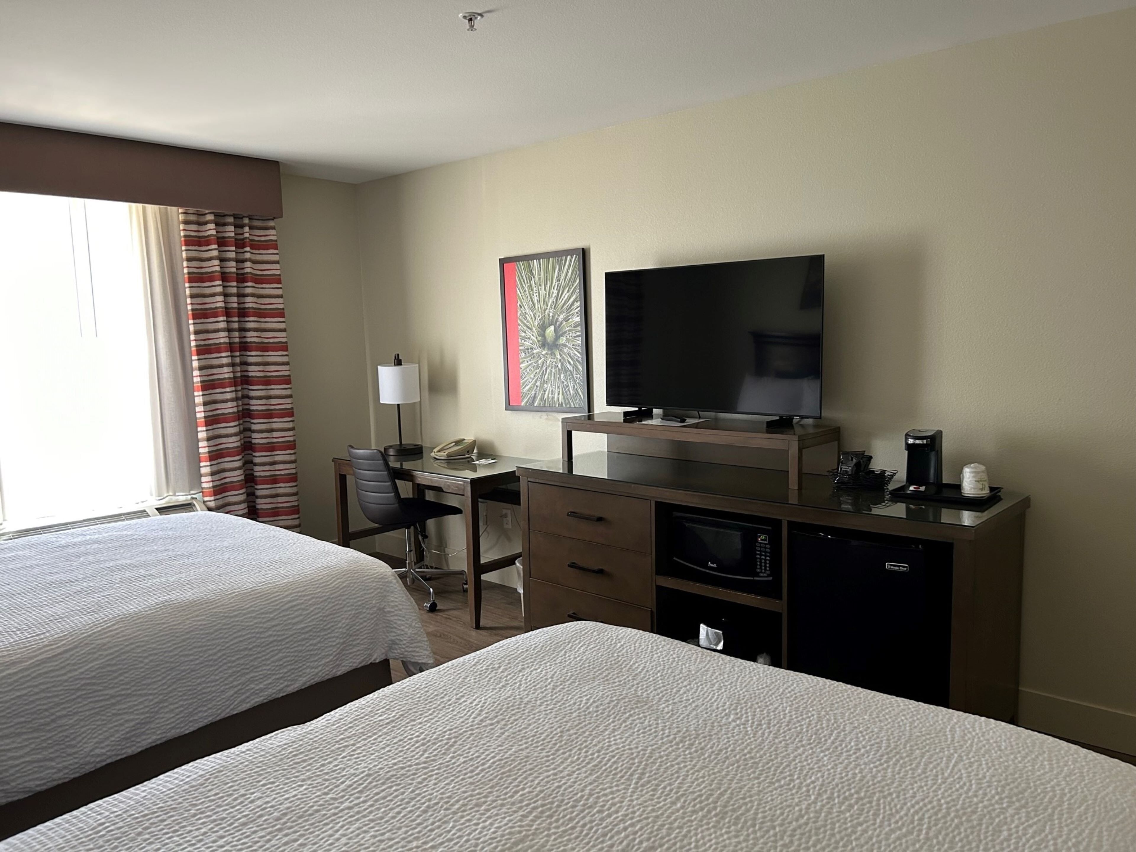 A hotel room with two beds, a desk with a chair, a television, a coffee maker, and a microwave.